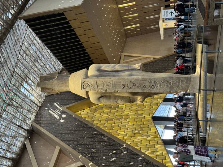 Giant ancient statue inside the Grand Egyptian Museum atrium with crowd of visitors below.