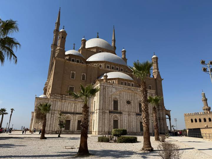 The grand Mosque of Muhammad Ali with towering minarets and palm trees under a clear blue Cairo sky.