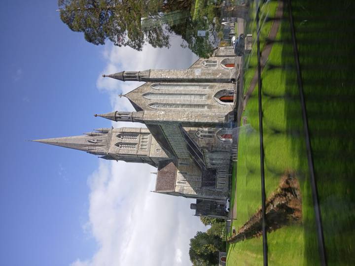 Tall stone cathedral with pointed spire and arched red doors set against a blue sky.