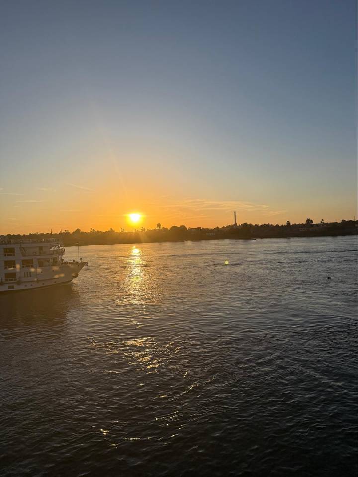 Orange sunset reflecting on the Nile River with cruise boat and palm silhouette.