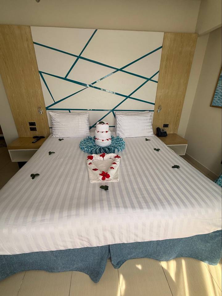 Hotel bed decorated with towel art, rose petals and phone on bedside table.