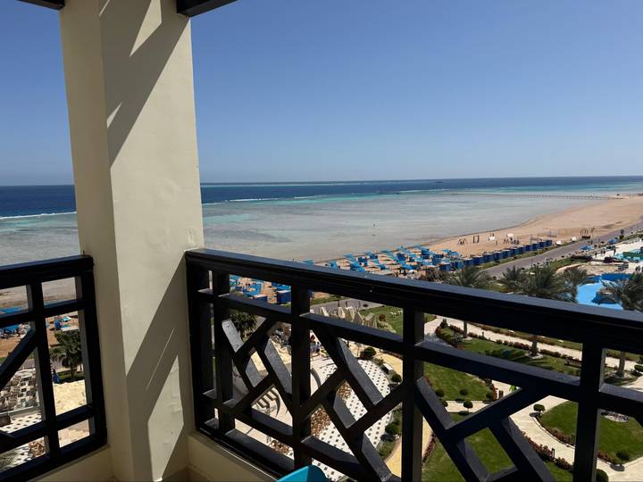 Balcony view over Red Sea shallows with rows of blue umbrellas and sandy beach.