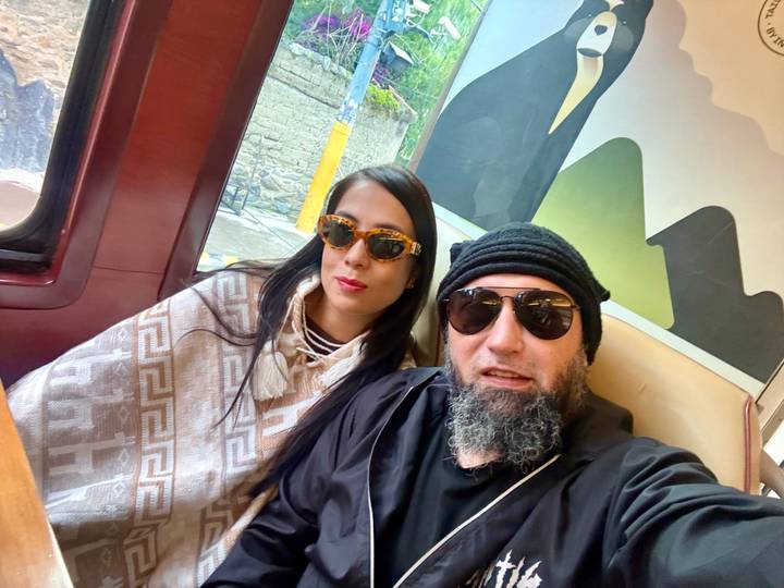 Couple seated inside a scenic train carriage wearing sunglasses and travel gear.