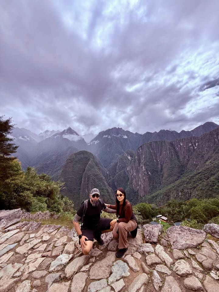 Couple standing before dramatic Andean mountain backdrop under moody clouds near Machu Picchu.