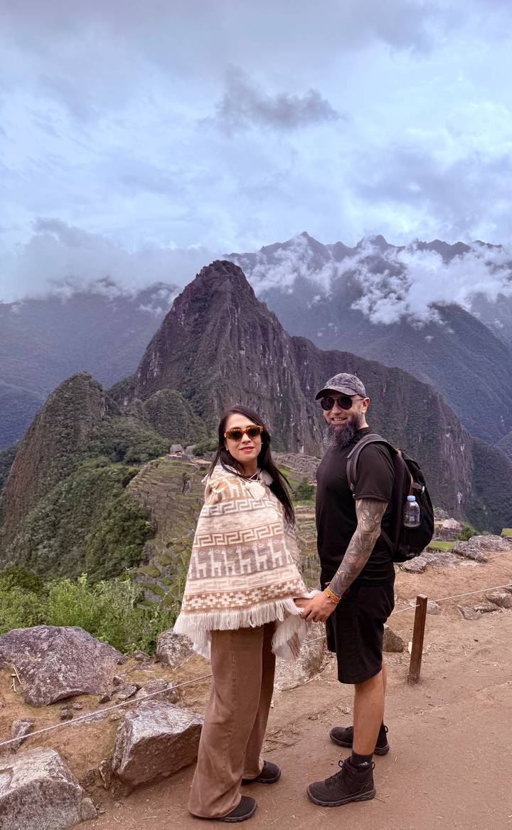 Smiling couple posing with the iconic Machu Picchu terraces and Huayna Picchu in the background.