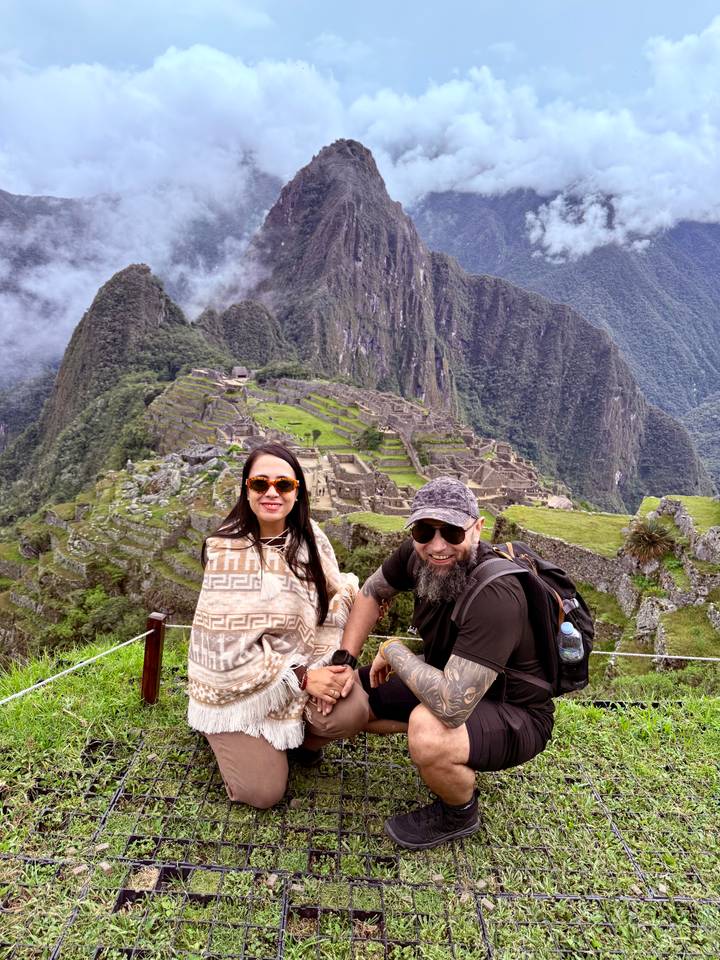 Couple crouching together at a viewpoint overlooking Machu Picchu's stone ruins.