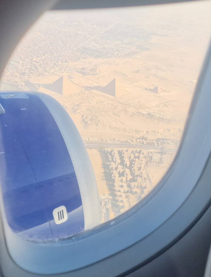 View from airplane window shows jet engine and the three Pyramids of Giza rising from the desert below.