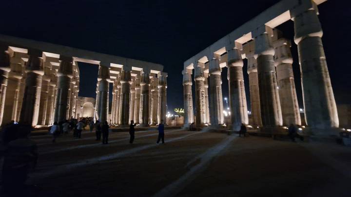 Nighttime view of Luxor Temple colonnade dramatically lit with visitors walking between soaring pillars.