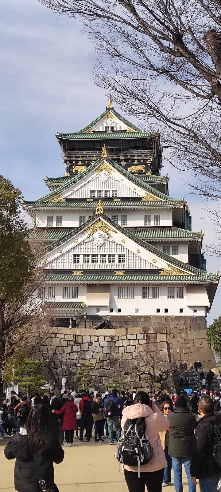Close-up of Osaka Castle’s ornate white walls, green roofs and gold detailing against a blue sky.