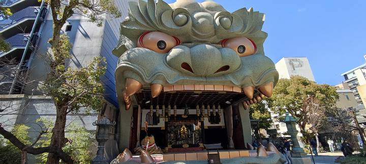 Large lion-head shaped shrine building with gaping mouth at Namba Yasaka Shrine under blue sky.