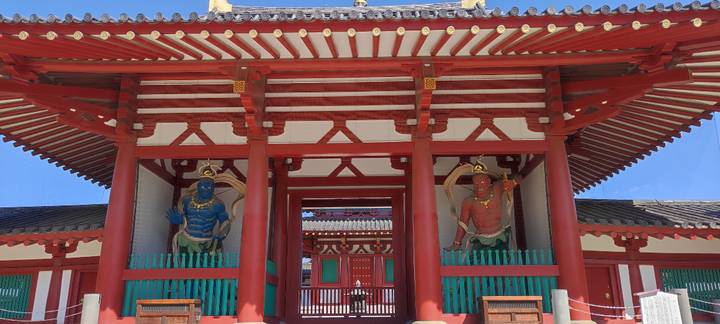 Symmetrical red temple gate with two guardian statues and bright blue sky overhead.
