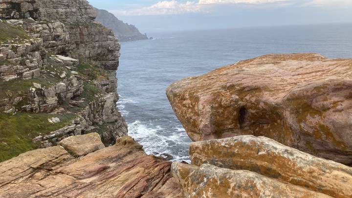 Sheer rocky coastline with waves crashing against the base and rugged cliffs extending into the distance.