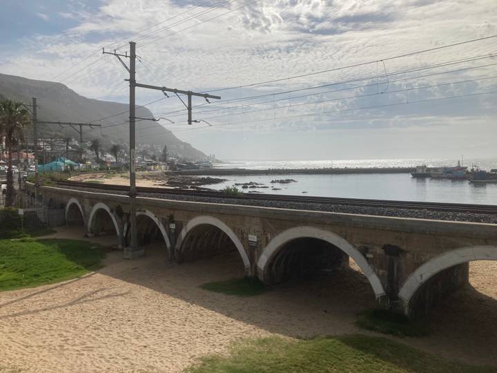Coastal railway viaduct with multiple arches beside sparkling sea and a mountain backdrop.