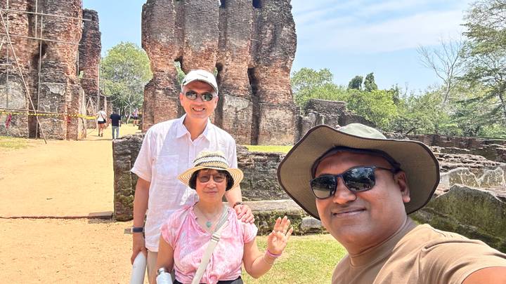 Selfie of guide and two visitors at ancient brick ruins under bright sunshine.