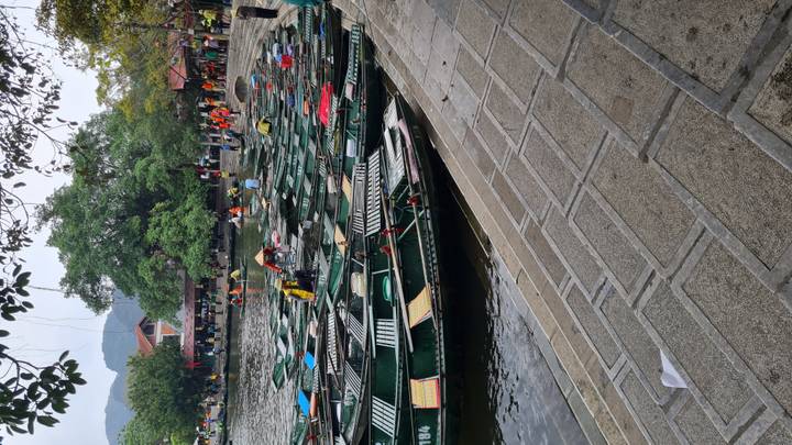 Dozens of green rowboats line the pier at Trang An with visitors preparing to board.
