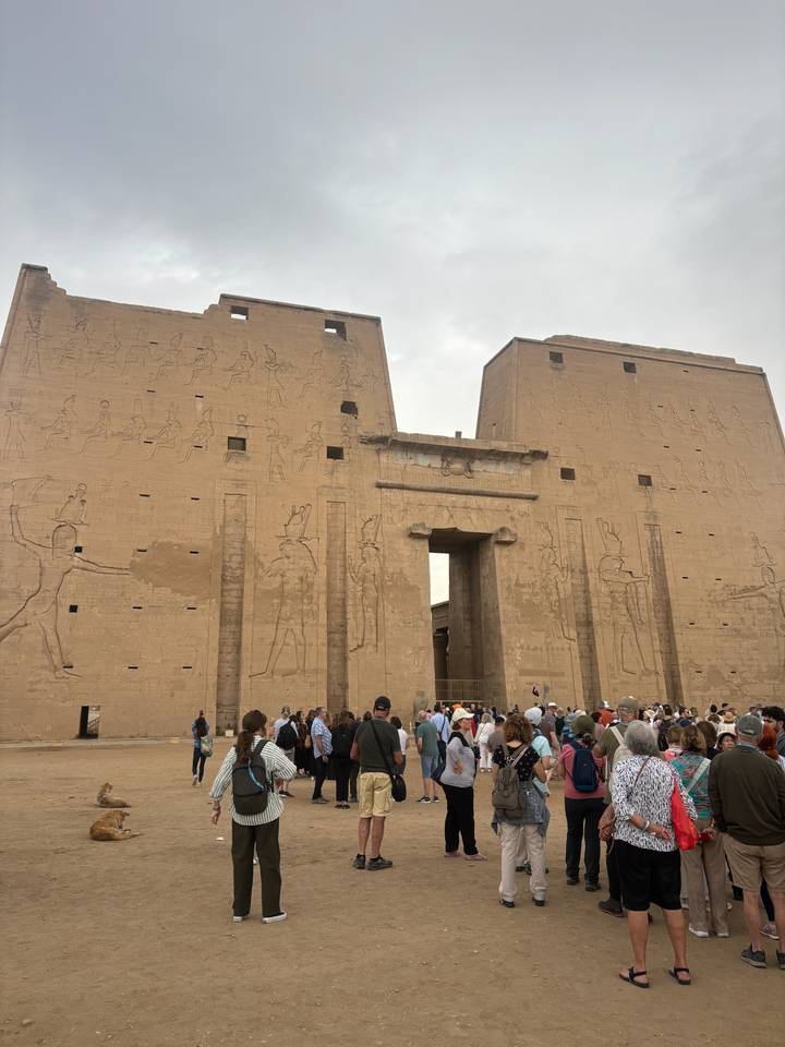 Crowd gathers at the massive sandstone entrance pylons of Edfu Temple covered in hieroglyphic carvings