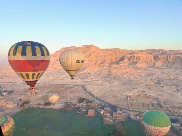 Colorful hot air balloons float above the desert cliffs and green fields of Luxor at sunrise