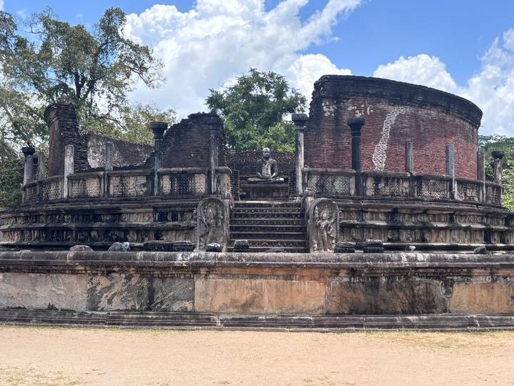 Ancient circular brick stupa of Polonnaruwa with seated Buddha statue at its centre.