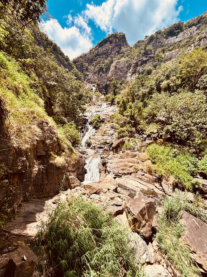 Tall multi-tiered waterfall cascading over rocky cliffs surrounded by lush green forest