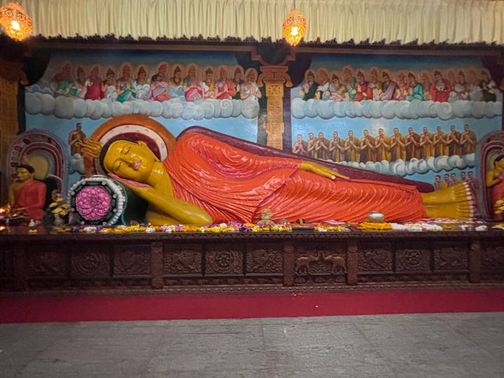 Colorful reclining Buddha statue inside an ornately painted temple hall with flower offerings