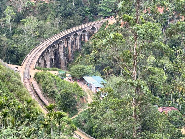 Historic Nine-Arch railway bridge curving through dense green jungle seen from above