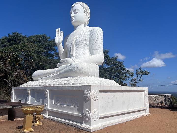 Large white seated Buddha statue on a pedestal against bright blue sky