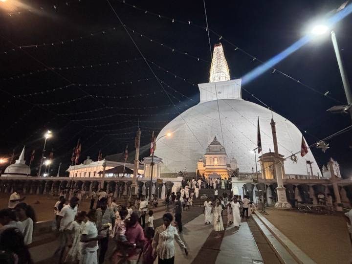 Nighttime gathering of devotees around a large illuminated stupa with festive lights