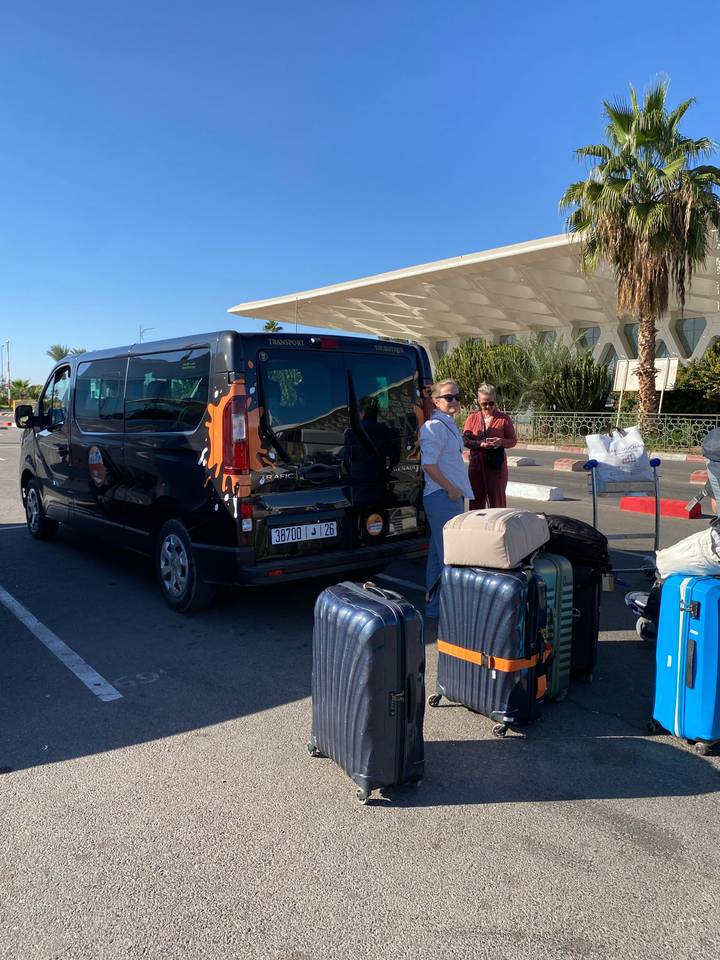 Tourists load luggage beside a branded minivan outside an airport terminal