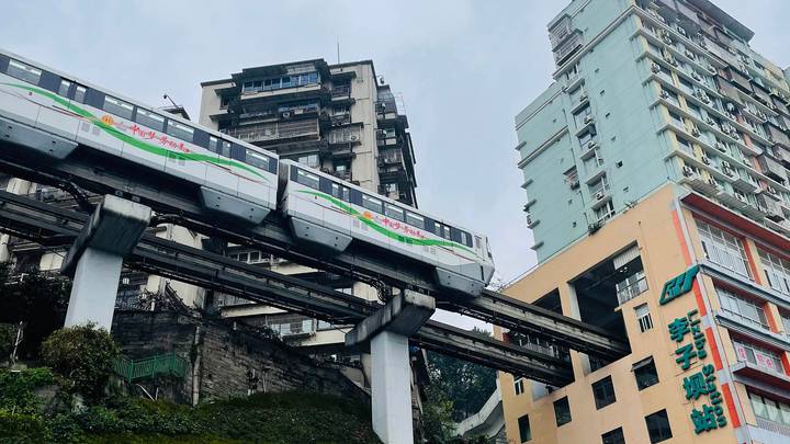 Urban monorail train passing through elevated tracks between high-rise buildings in Chongqing.