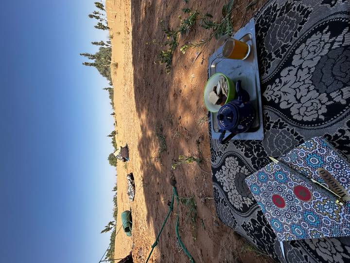 Moroccan tea set and snacks placed on patterned carpet with sandy desert beyond.