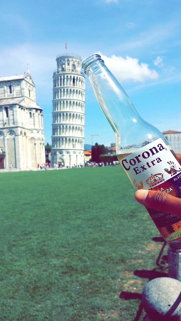 Main tenant une bouteille de bière Corona avec la Tour de Pise en arrière-plan.