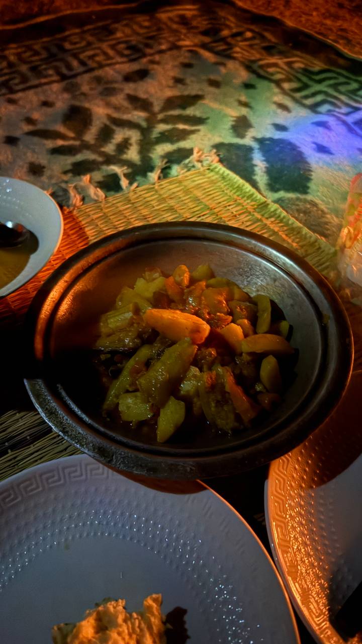 Close-up of a steaming earthenware dish filled with vegetables and sauce under low warm lighting.