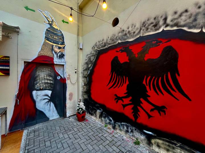 Street art mural depicting historical Albanian figure and red double-headed eagle flag emblem.