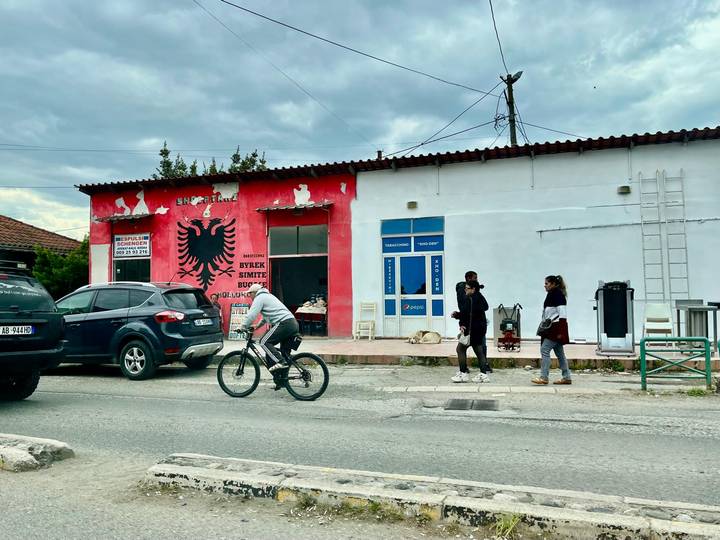 Small town street with cyclist passing by a building painted with Albanian eagle symbol.