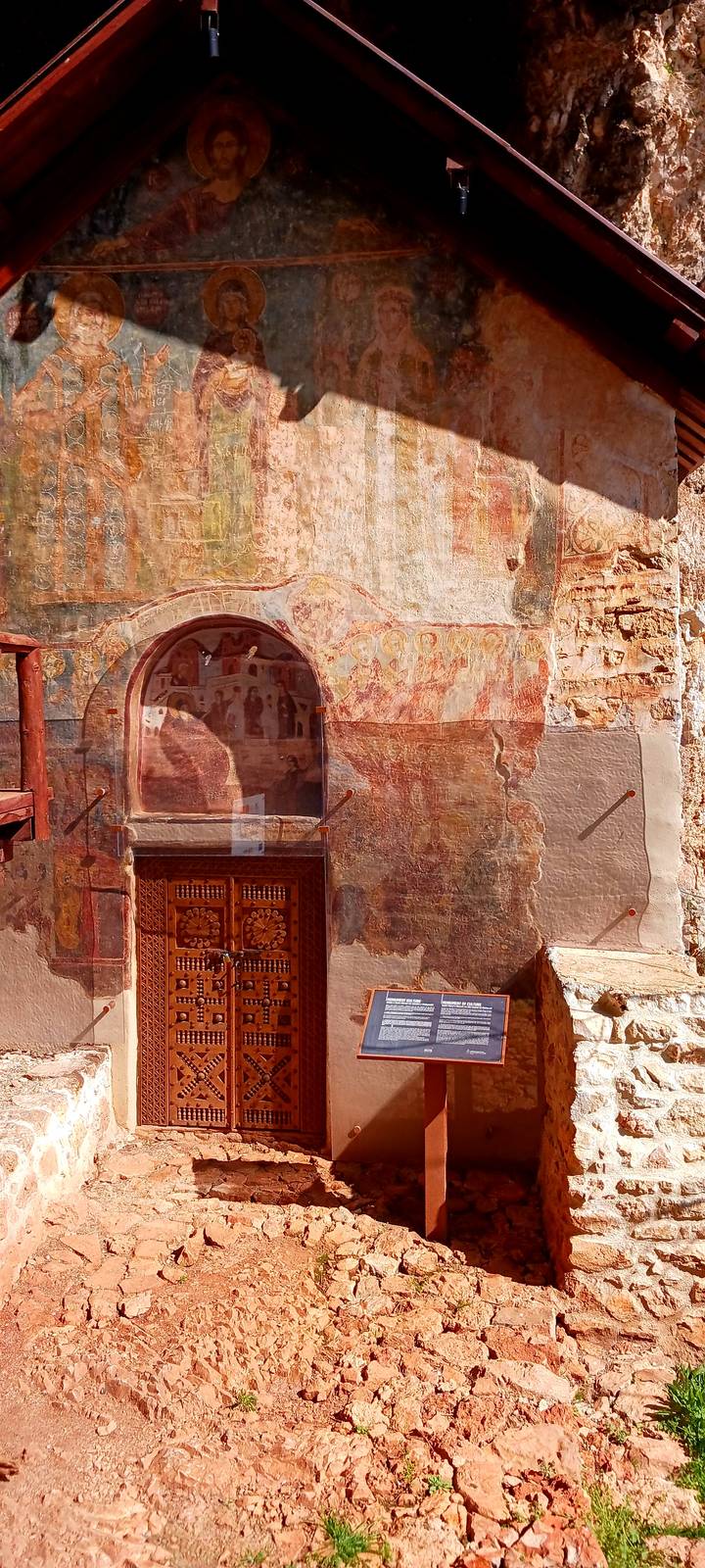 Aged frescoes and ornate wooden door inside an old Albanian church or monastery.