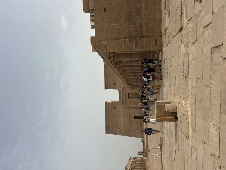 Tourists exploring a vast sandstone temple complex with tall columns in the Egyptian desert.