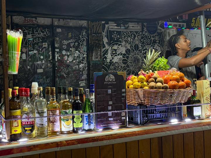 Colorful bar stall displaying fresh fruit and liquor bottles with a bartender preparing drinks.