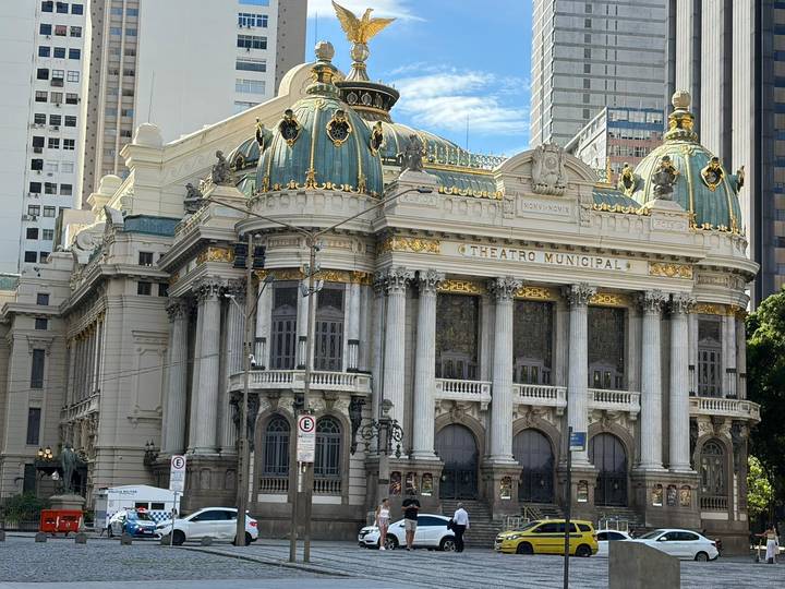 Daytime view of ornate green-roofed Theatro Municipal against a blue sky.