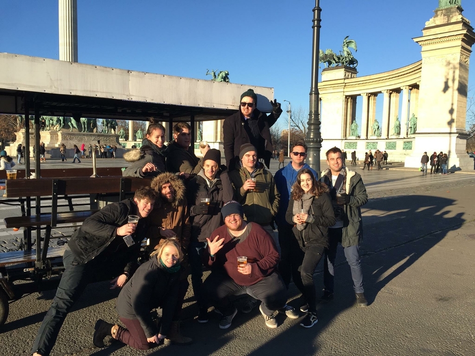 Groupe de personnes buvant un verre sur une place publique avec des statues.
