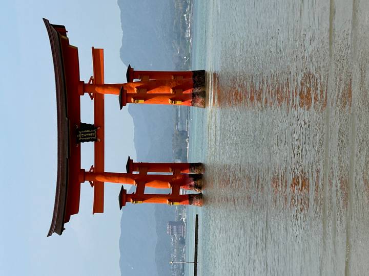 Iconic vermilion Itsukushima floating torii gate rising from calm sea with mountains behind.