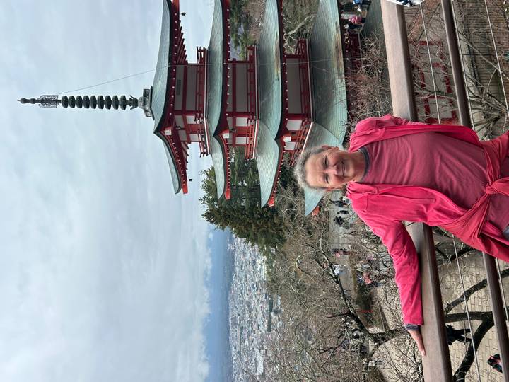 Visitor posing before red Chureito Pagoda with cityscape and distant mountains.