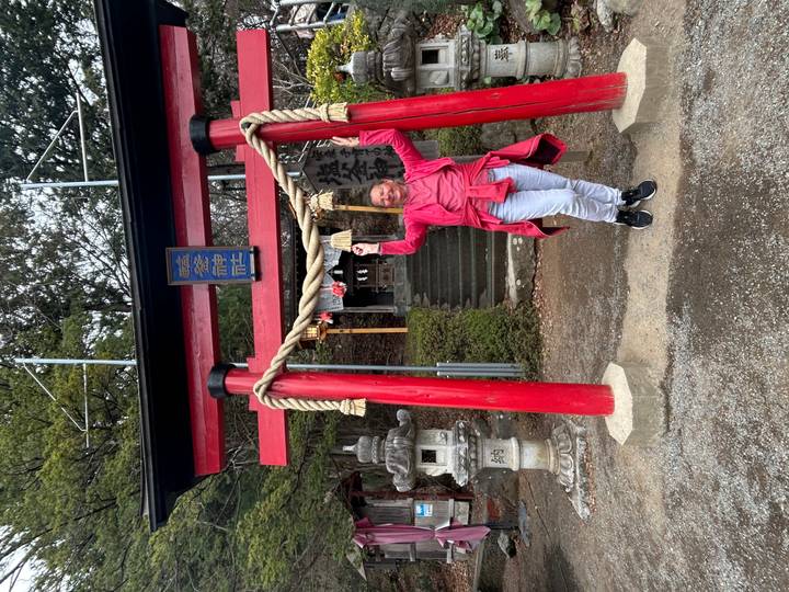 Traveler celebrating beneath small red torii gate at forest shrine.