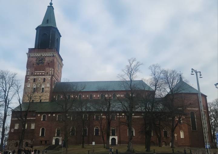 Brick Turku Cathedral with tall clock tower set against an overcast sky and bare winter trees.