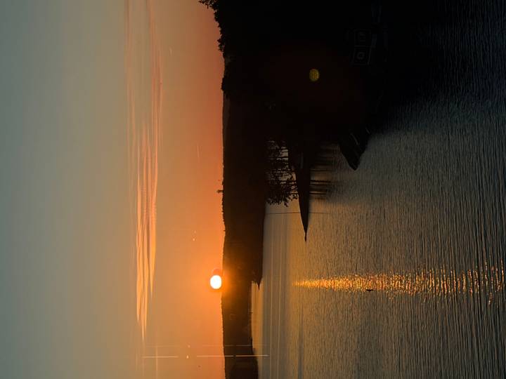 Serene sunset over forested islands with golden reflections on still water viewed from a vessel.