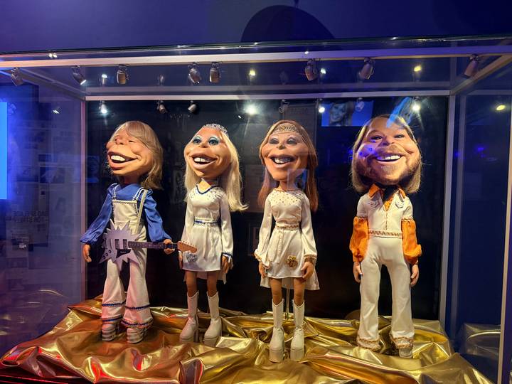Caricatured ABBA band member puppets displayed in glass cases at a museum exhibit.