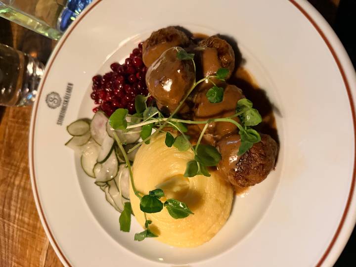 Traditional Swedish meatballs with mashed potatoes, lingonberries and pickled cucumber served on a white plate.