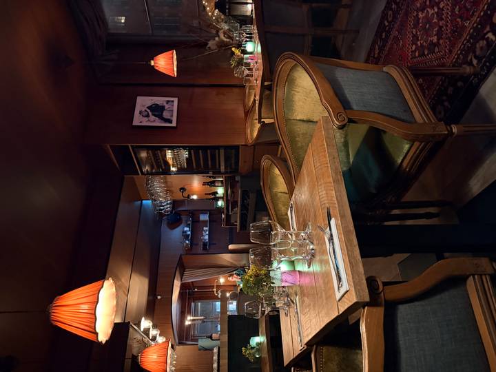 Cozy, dimly-lit Scandinavian restaurant interior with set tables, wine glasses and warm pendant lights.