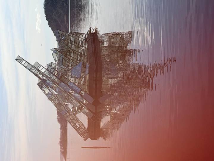 Glass-and-steel sculpture rising from calm harbor water with its reflection shimmering
