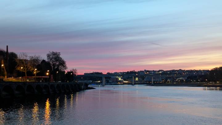 Soft pastel sunset over calm river near Porto with lights beginning to twinkle.