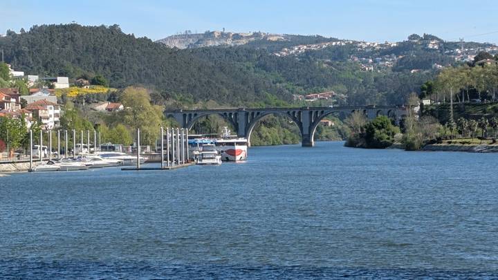 Arched stone bridge spanning the Douro River with cruise boats and forested hills beyond.